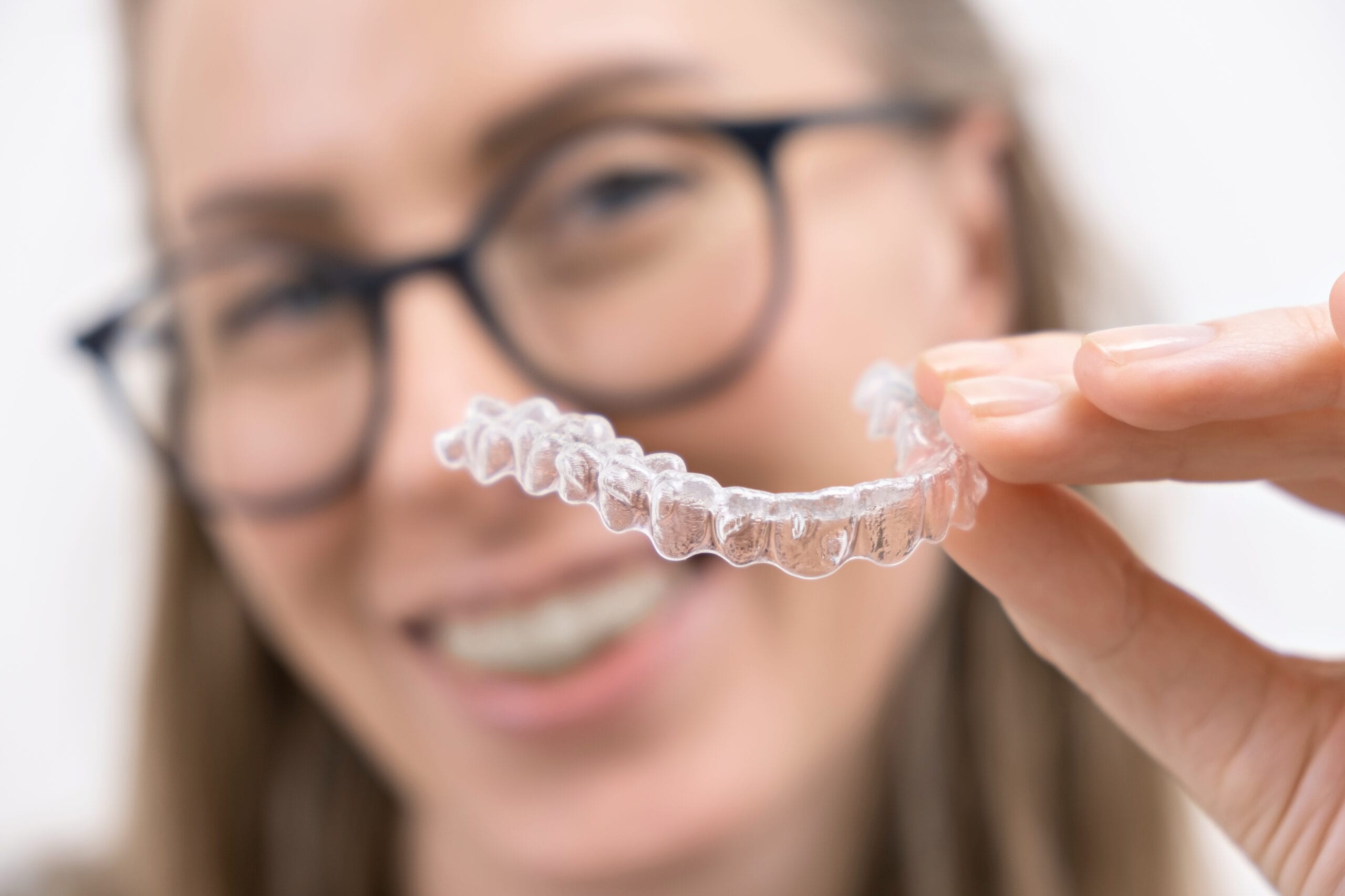 smiling woman using clear plastic removable braces aligner or whitening tray. dental orthodontic care.